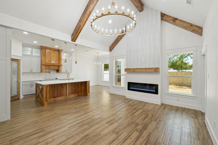 Unfurnished living room featuring light hardwood / wood-style flooring, a healthy amount of sunlight, beam ceiling, and high vaulted ceiling