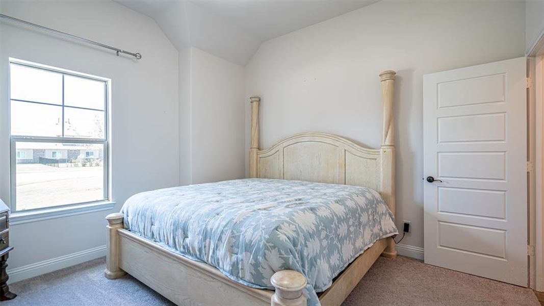 Vaulted ceiling bedroom featuring a large window, neutral carpeting, and a five-panel interior door