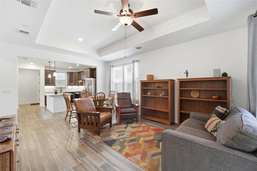 Living area featuring light wood finished floors, a raised ceiling, a ceiling fan, and recessed lighting