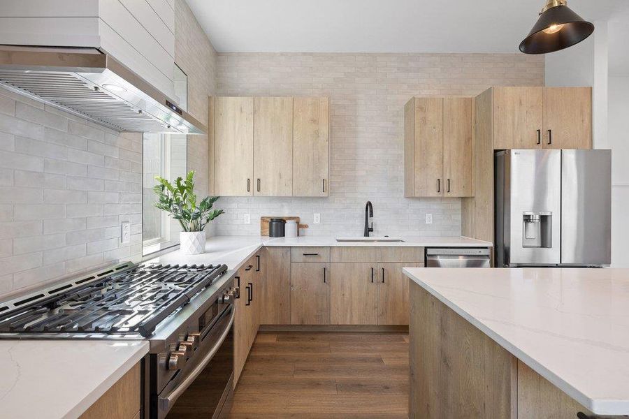 Kitchen featuring stainless steel appliances, light brown wood grain cabinets with upgraded tile backsplash to ceiling