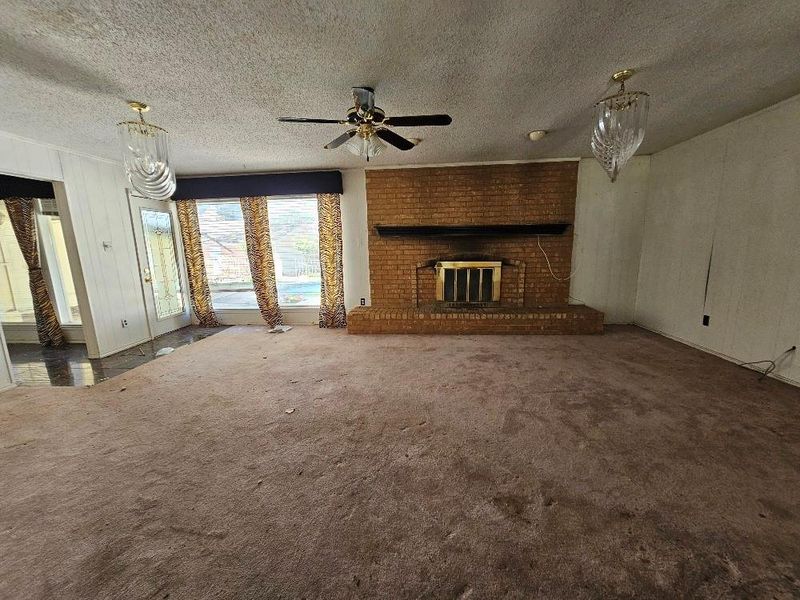 Unfurnished living room featuring a fireplace, a textured ceiling, dark carpet, and a ceiling fan Unfurnished living room featuring a fireplace, a textured ceiling, dark carpet, and a ceiling fan