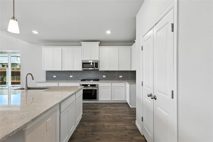 Kitchen with white cabinetry, stainless steel appliances, dark wood finished floors, pendant lighting, and light stone counters