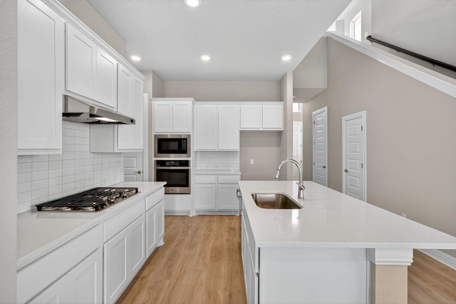 Kitchen with light wood-type flooring, decorative backsplash, a kitchen island with sink, appliances with stainless steel finishes, and white cabinets Kitchen with light wood-type flooring, decorative backsplash, a kitchen island with sink, appliances with stainless steel finishes, and white cabinets