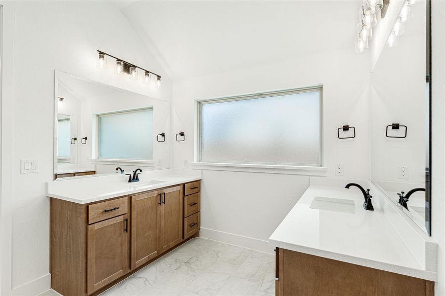 Bathroom with dual wood vanities, white quartz countertops, black fixtures, and marble tile floors Bathroom with dual wood vanities, white quartz countertops, black fixtures, and marble tile floors