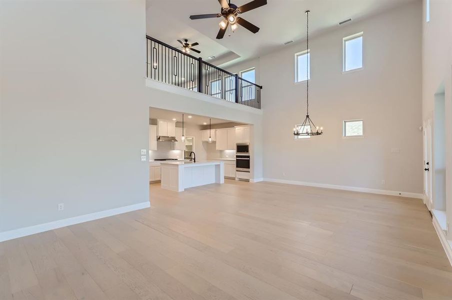 Unfurnished living room with ceiling fan with notable chandelier, light wood-type flooring, and a towering ceiling