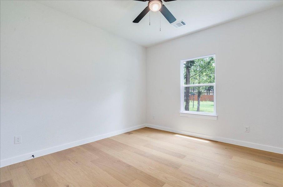 Natural light bathes this secondary bedroom with rich hardwood flooring and a functional ceiling fan.