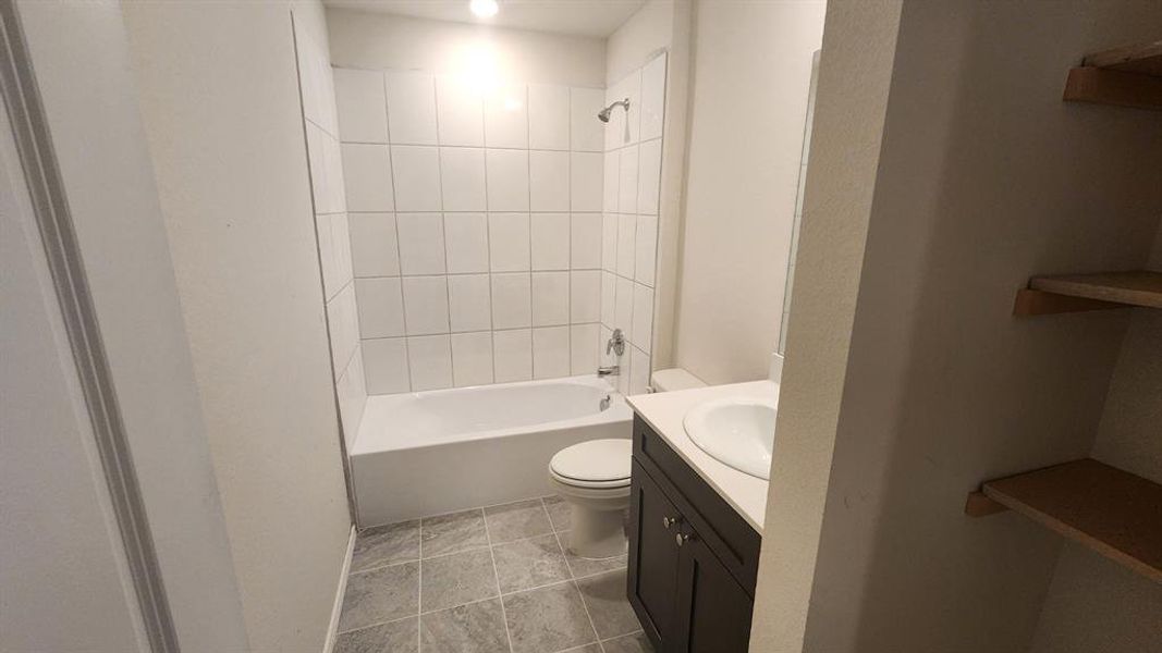 Bathroom featuring a white bathtub with tile surround, a dark wood-finish vanity with an integrated sink, a matching toilet, and tile flooring