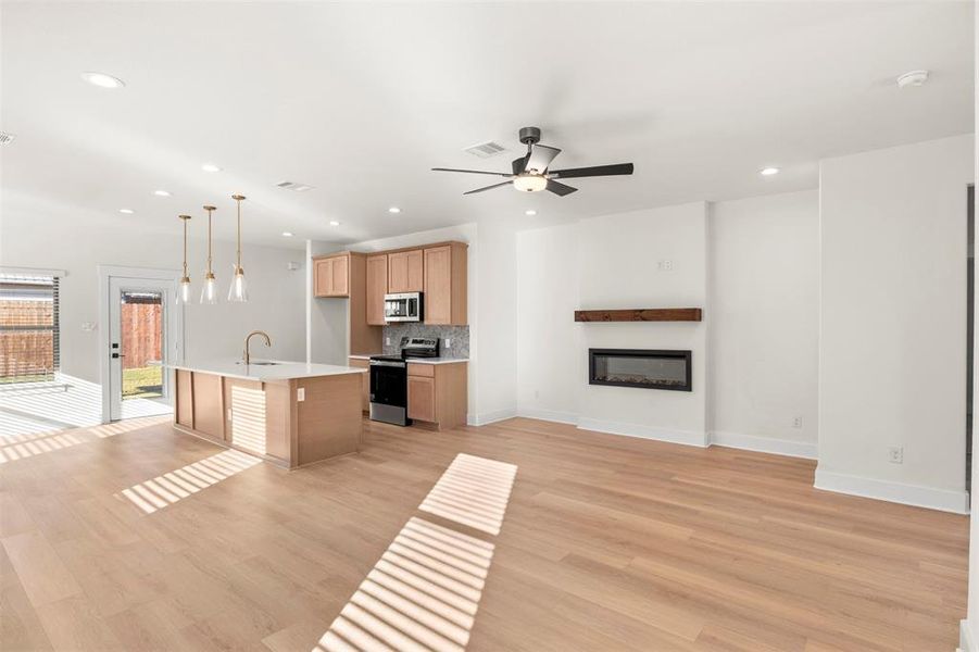 Kitchen featuring open floor plan, appliances with stainless steel finishes, decorative light fixtures, a glass covered fireplace, and light wood finished floors