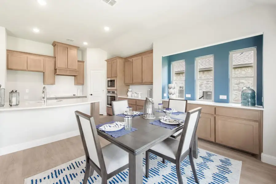Dining area with four-seat table adjacent to kitchen with light wood cabinets and blue accent wall
