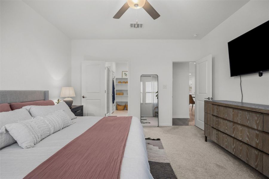 Spacious bedroom featuring light-colored carpeting, a contemporary ceiling fan, built-in closet shelving, and a flat-panel television wall mount