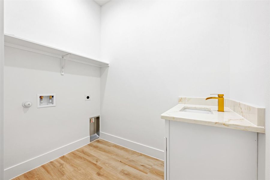 Dedicated laundry space featuring wood-finish flooring, a built-in shelf, and a corner vanity with a light-toned countertop and a gold-finish faucet
