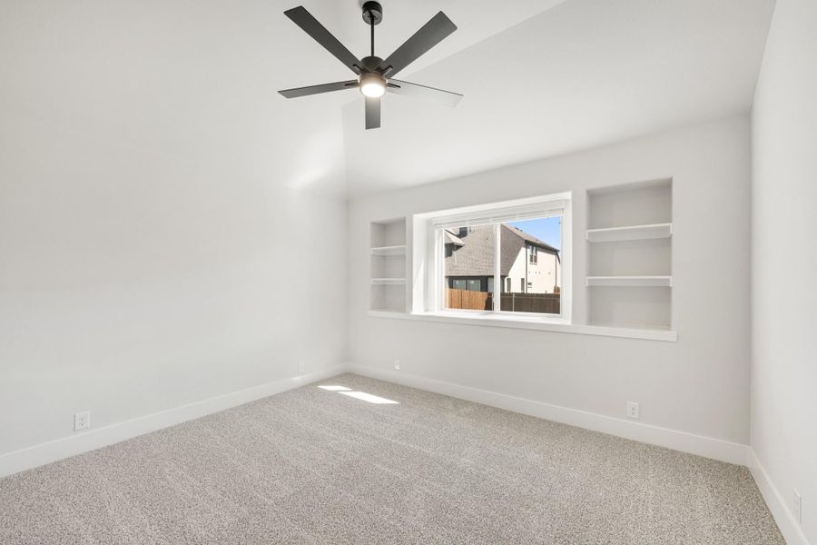 Empty bedroom with carpet, vaulted ceiling, ceiling fan, and built-in shelves flanking a window