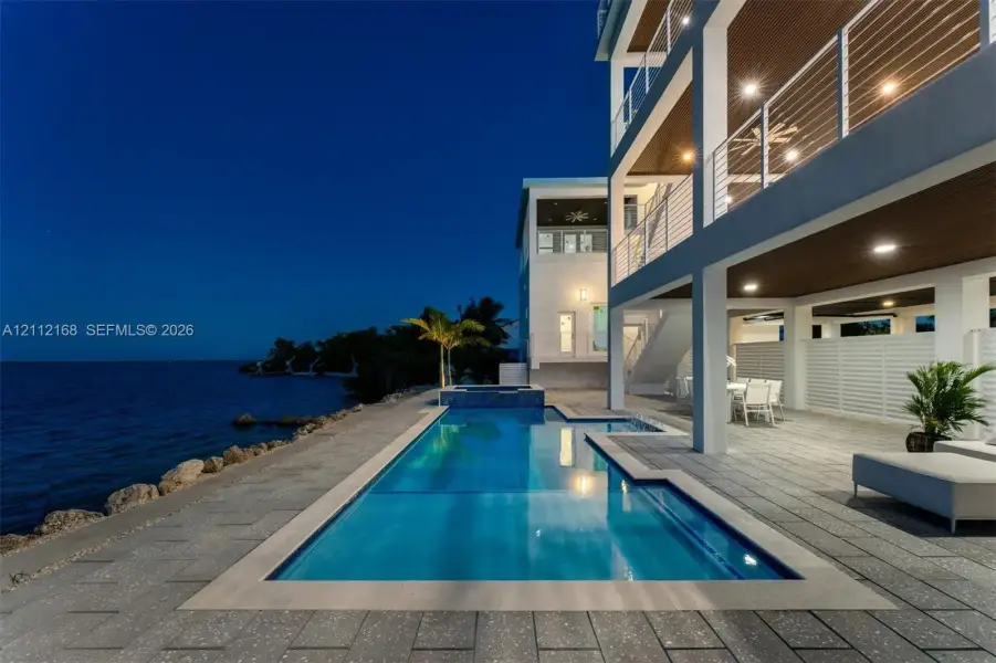 Multi-level structure featuring expansive covered balconies with horizontal cable railings, tile-surround swimming pool, integrated spa, and expansive stone-paved patio Multi-level structure featuring expansive covered balconies with horizontal cable railings, tile-surround swimming pool, integrated spa, and expansive stone-paved patio