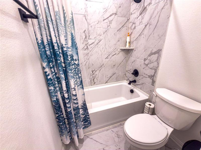 Bathroom with a textured wall, marble look tiles, and shower / bath combination with curtain