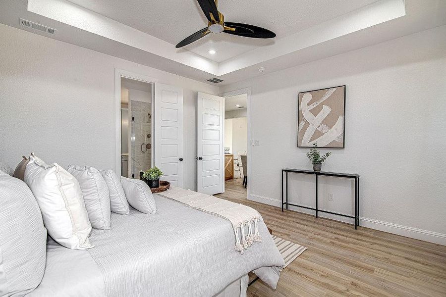 Bedroom with a raised ceiling, baseboards, visible vents, and light wood finished floors