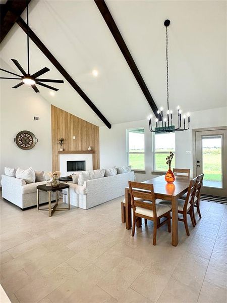 Dining space with beam ceiling, high vaulted ceiling, a chandelier, and a large fireplace