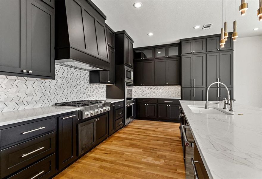 Kitchen featuring appliances with stainless steel finishes, sink, hanging light fixtures, light hardwood / wood-style floors, and decorative backsplash