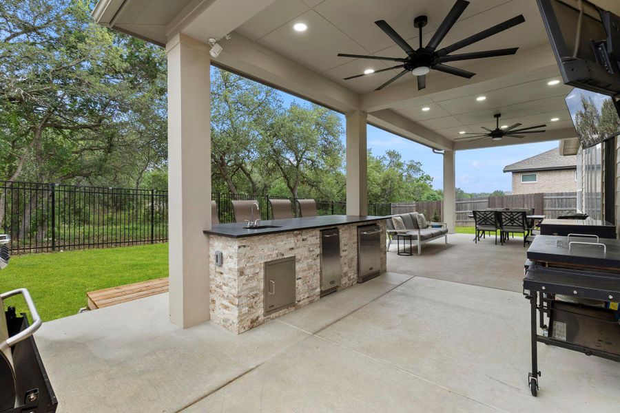 Expansive outdoor living area featuring a built-in stone-clad island with integrated sink and stainless steel appliances