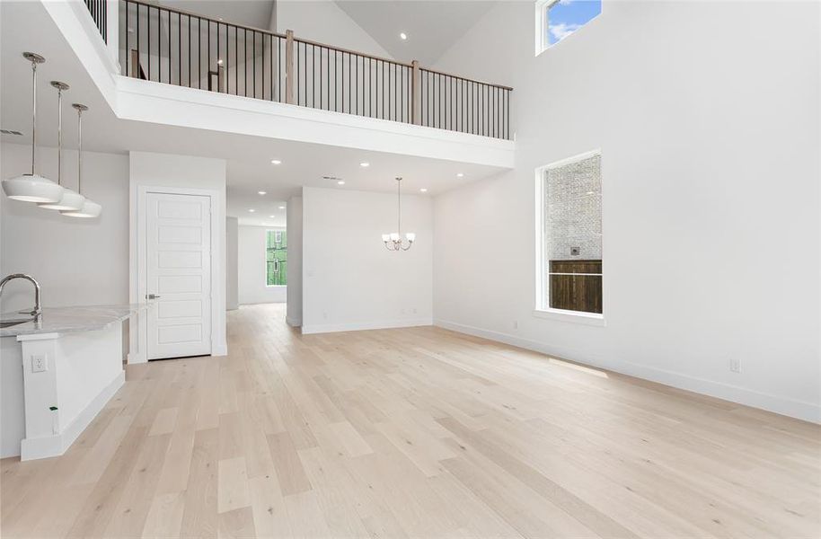 Unfurnished living room with a towering ceiling, sink, a chandelier, and light hardwood / wood-style floors