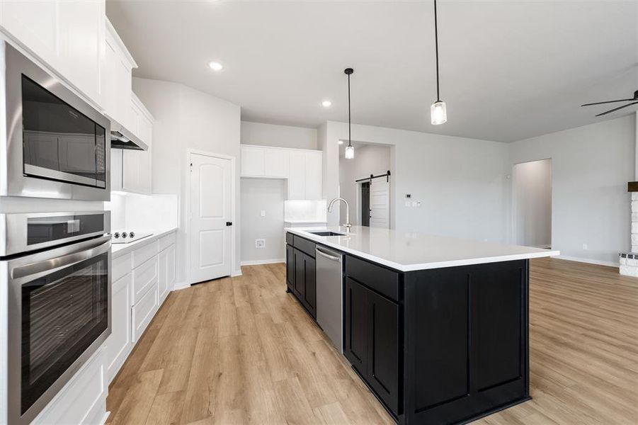 Kitchen featuring dark cabinetry, a barn door, stainless steel appliances, white cabinetry, and hanging light fixtures Kitchen featuring dark cabinetry, a barn door, stainless steel appliances, white cabinetry, and hanging light fixtures