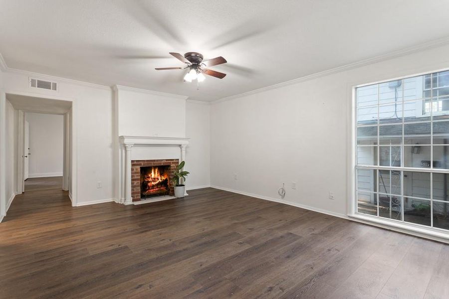 Unfurnished living room with a ceiling fan, dark wood-type flooring, a brick fireplace, ornamental molding, and baseboards