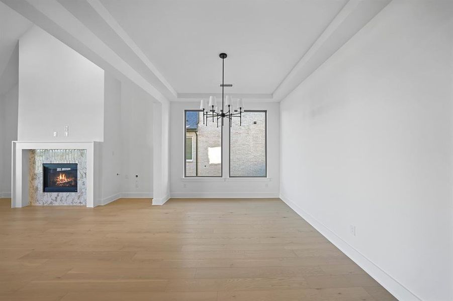 Unfurnished living room featuring light wood-style floors, a raised ceiling, a premium fireplace, and a chandelier