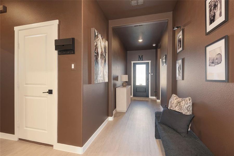 Hallway featuring light wood-finish flooring, white baseboards, and a white two-panel door with black hardware Hallway featuring light wood-finish flooring, white baseboards, and a white two-panel door with black hardware