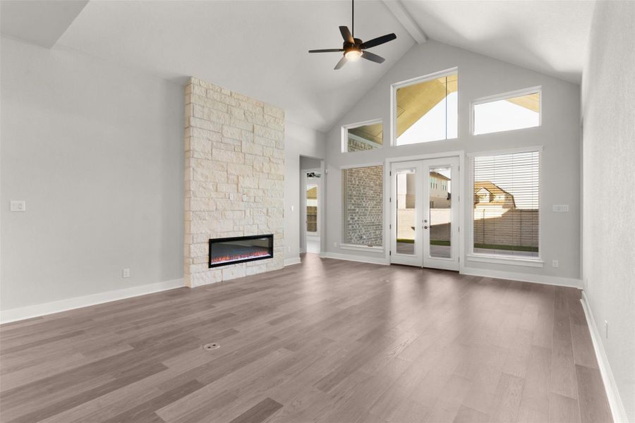 Unfurnished living room featuring high vaulted ceiling, french doors, beamed ceiling, a ceiling fan, and a stone fireplace