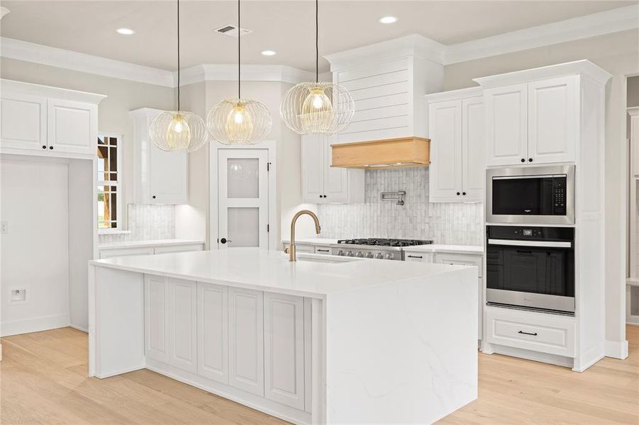 Kitchen with tasteful backsplash, appliances with stainless steel finishes, light wood finished floors, crown molding, and white cabinets Kitchen with tasteful backsplash, appliances with stainless steel finishes, light wood finished floors, crown molding, and white cabinets