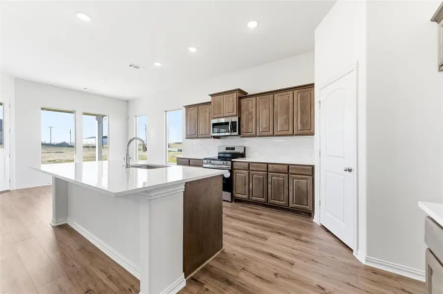 Kitchen featuring stainless steel appliances, a kitchen island with sink, tasteful backsplash, light wood-type flooring, and recessed lighting