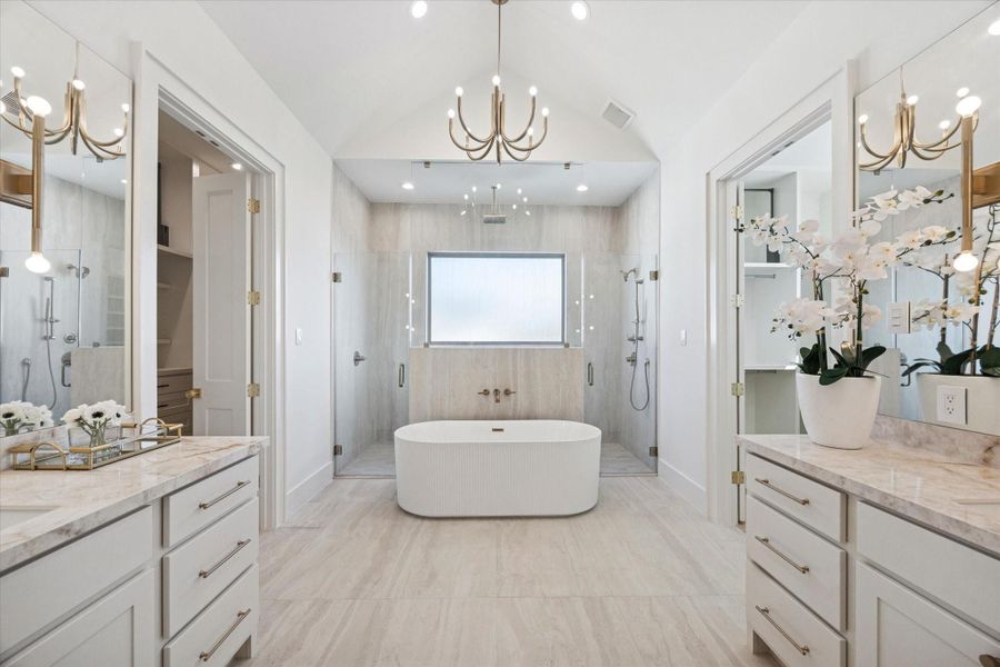 Luxurious primary bath featuring a vaulted ceiling, dual vanities, a soaking tub with fluted detailing, and a spacious walk-in shower with multiple shower heads. Two custom walk-in closets with built-ins and porcelain countertops complete the space—truly a dream setting to start and end your day.