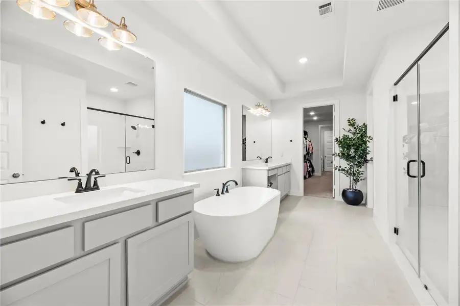 Enjoy a daily dose of luxury in the owner’s ensuite, complete with a freestanding soaking tub, separate glass-enclosed shower, dual sink vanities with framed mirrors and chic lighting, and direct access to an oversized walk-in closet and utility room for unmatched convenience.