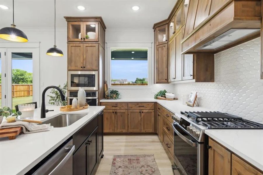 Kitchen with stainless steel appliances, glass insert cabinets, hanging light fixtures, two tone cabinets, and light wood-style flooring