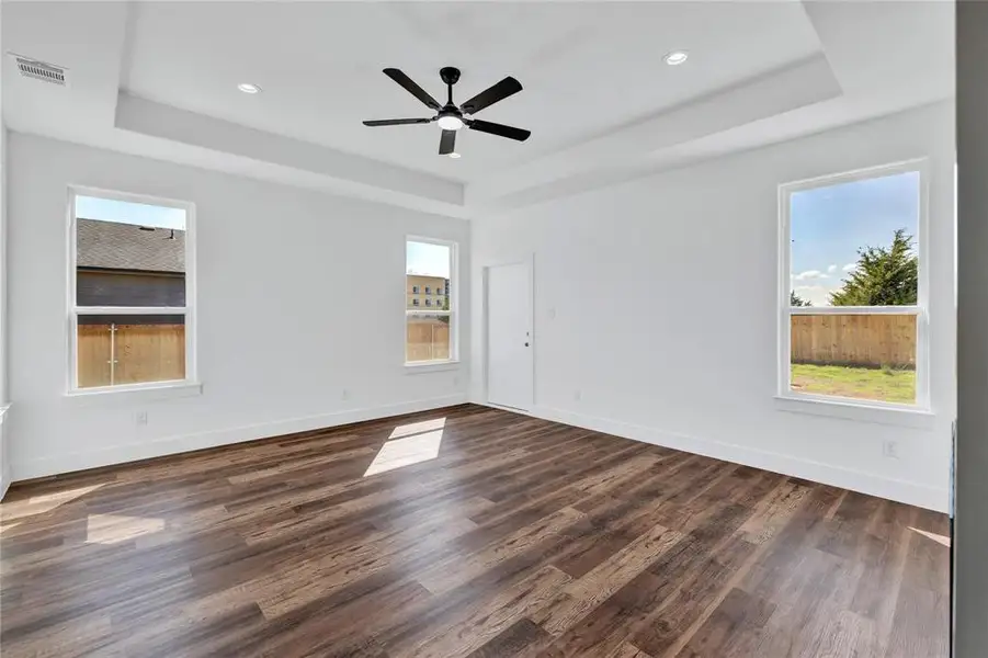 Unfurnished room featuring plenty of natural light, dark wood-style flooring, ceiling fan, a raised ceiling, and recessed lighting