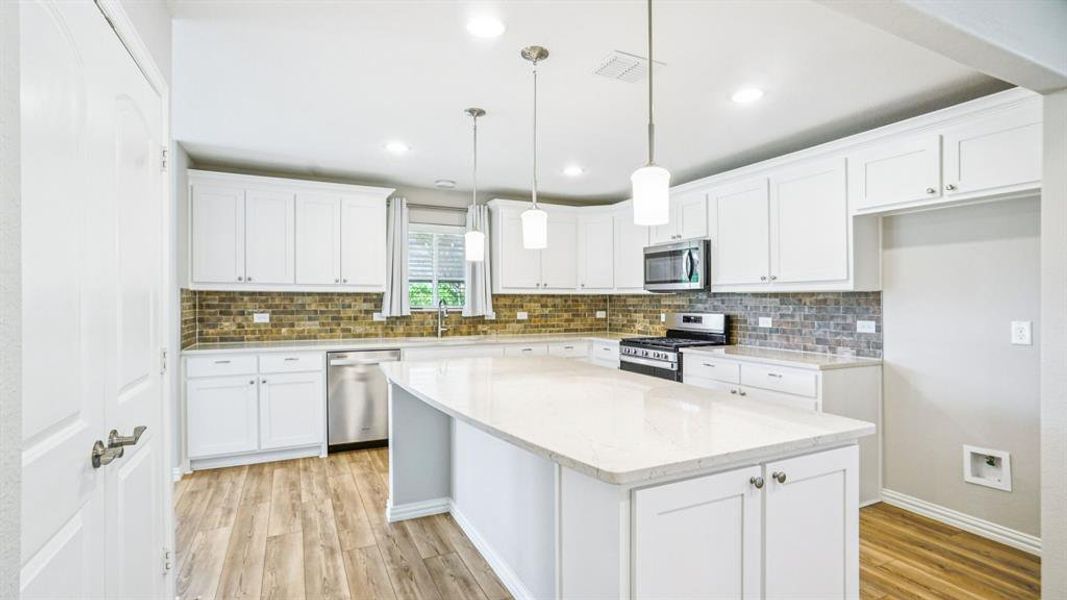Kitchen featuring a kitchen island, hanging light fixtures, appliances with stainless steel finishes, light wood-style flooring, and tasteful backsplash Kitchen featuring a kitchen island, hanging light fixtures, appliances with stainless steel finishes, light wood-style flooring, and tasteful backsplash