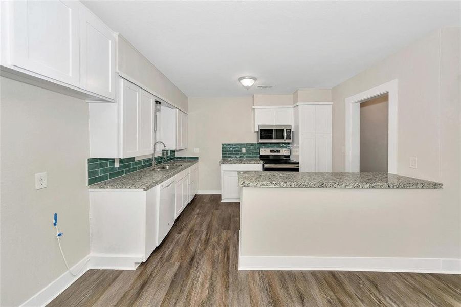 Kitchen featuring stainless steel appliances, dark wood-style floors, decorative backsplash, white cabinets, and light stone countertops Kitchen featuring stainless steel appliances, dark wood-style floors, decorative backsplash, white cabinets, and light stone countertops