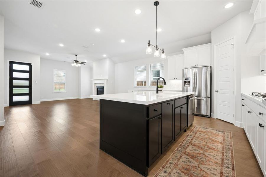 Open-concept kitchen featuring a dark island with white quartz countertops, stainless steel appliances, and white cabinetry