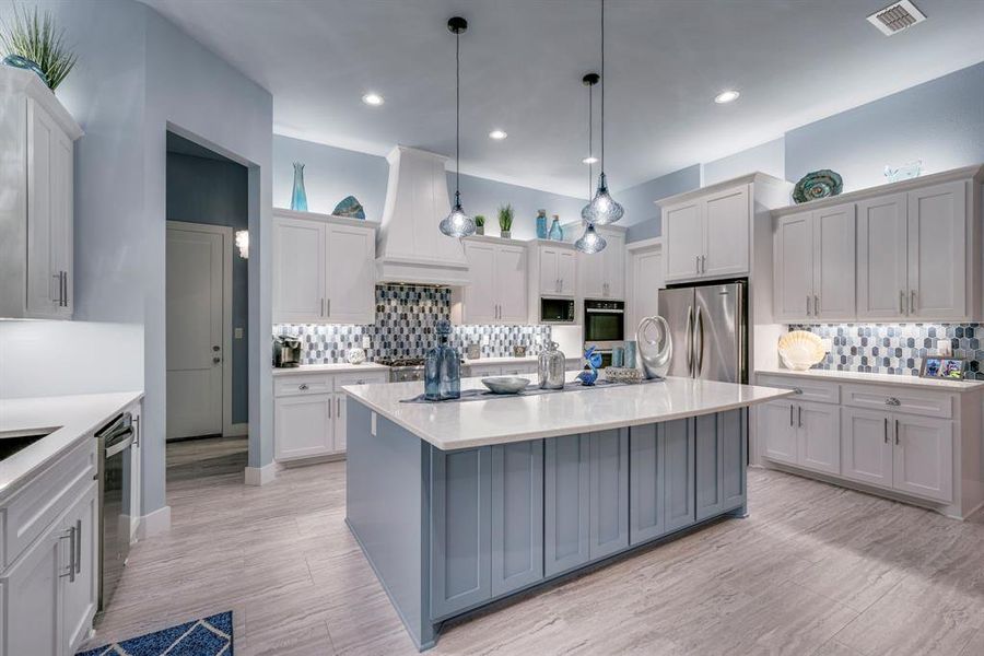 Kitchen featuring a center island, hanging light fixtures, premium range hood, decorative backsplash, and appliances with stainless steel finishes