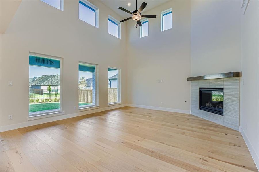 Unfurnished living room with a tile fireplace, light wood-type flooring, ceiling fan, and a high ceiling