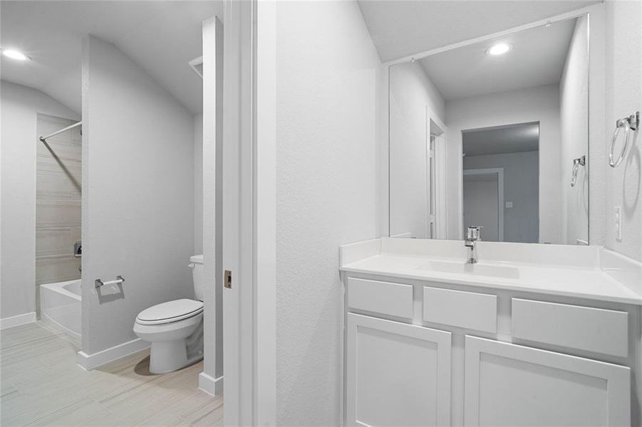 Secondary bath is a jack and jill bathroom featuring tile flooring, bath/shower combo with tile surround, white stained wood cabinets, beautiful light countertops, mirror, sleek fixtures and modern finishes.