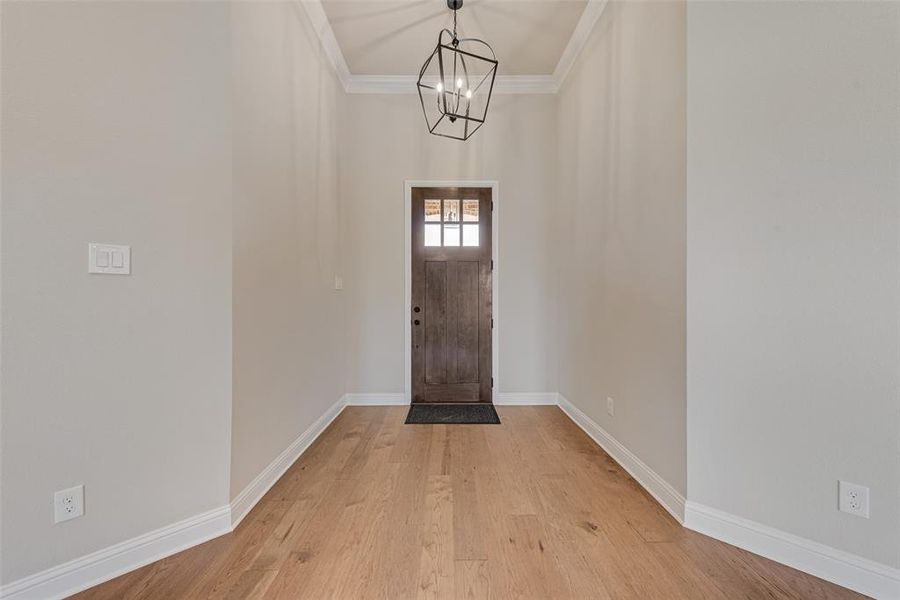 Entryway featuring light wood-style floors, a chandelier, and crown molding