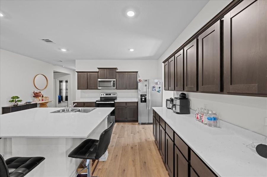 Kitchen featuring dark brown cabinets, light wood finished floors, stainless steel appliances, light stone countertops, and recessed lighting Kitchen featuring dark brown cabinets, light wood finished floors, stainless steel appliances, light stone countertops, and recessed lighting