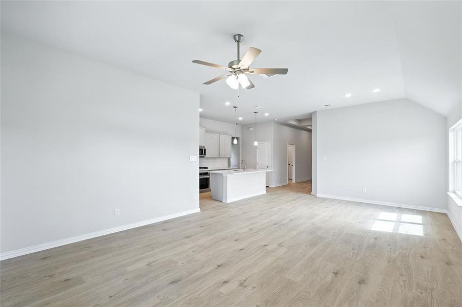 Unfurnished living room featuring light wood finished floors, vaulted ceiling, and ceiling fan Unfurnished living room featuring light wood finished floors, vaulted ceiling, and ceiling fan