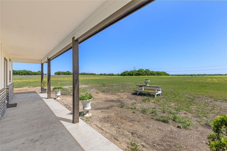 Expansive covered concrete patio with dark wood-finish support columns, offering a broad open field landscape