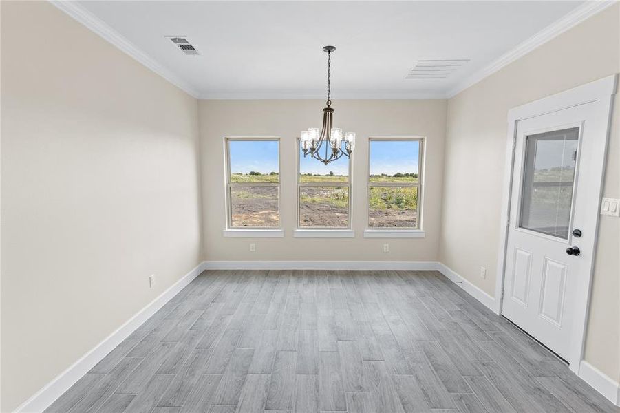 Unfurnished dining area with ornamental molding, a notable chandelier, and light hardwood / wood-style floors