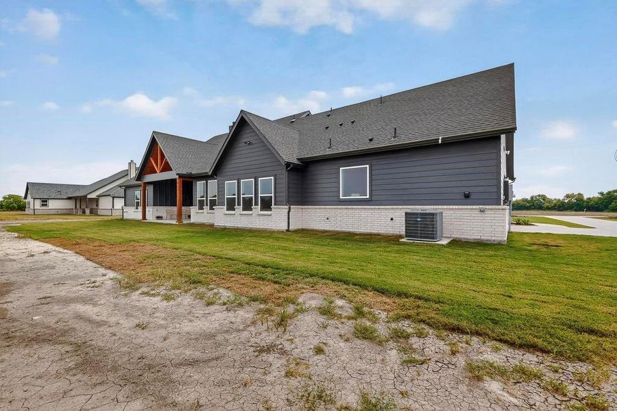 Rear view of house with a yard, brick siding, a shingled roof, and a patio