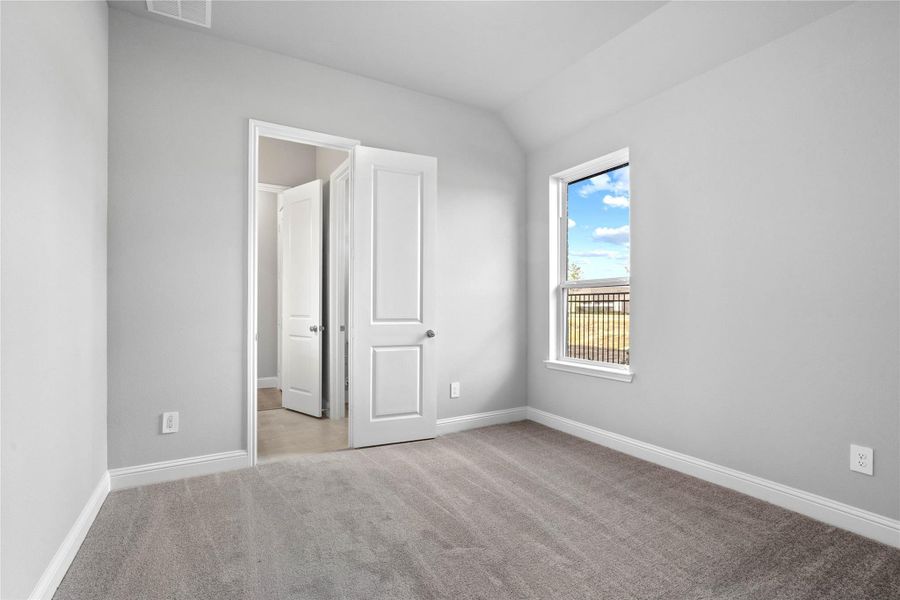 This secondary bedroom features plush carpet flooring, neutral toned walls, a large window, walk-in closet, and an access door to a shared secondary bathroom.