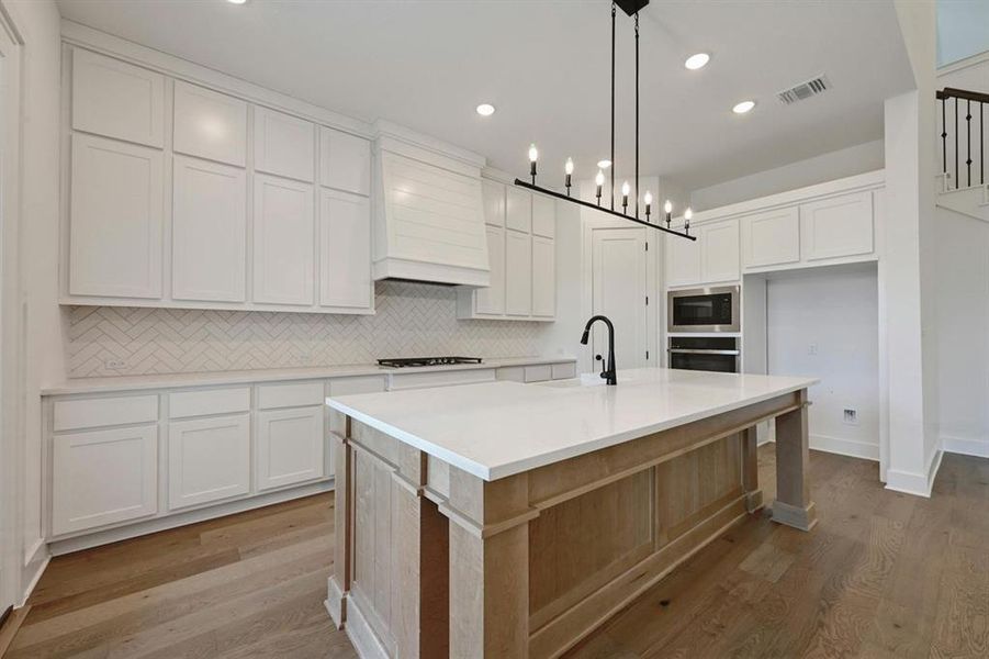 Kitchen featuring decorative backsplash, white cabinets, light wood-type flooring, a center island with sink, and recessed lighting Kitchen featuring decorative backsplash, white cabinets, light wood-type flooring, a center island with sink, and recessed lighting
