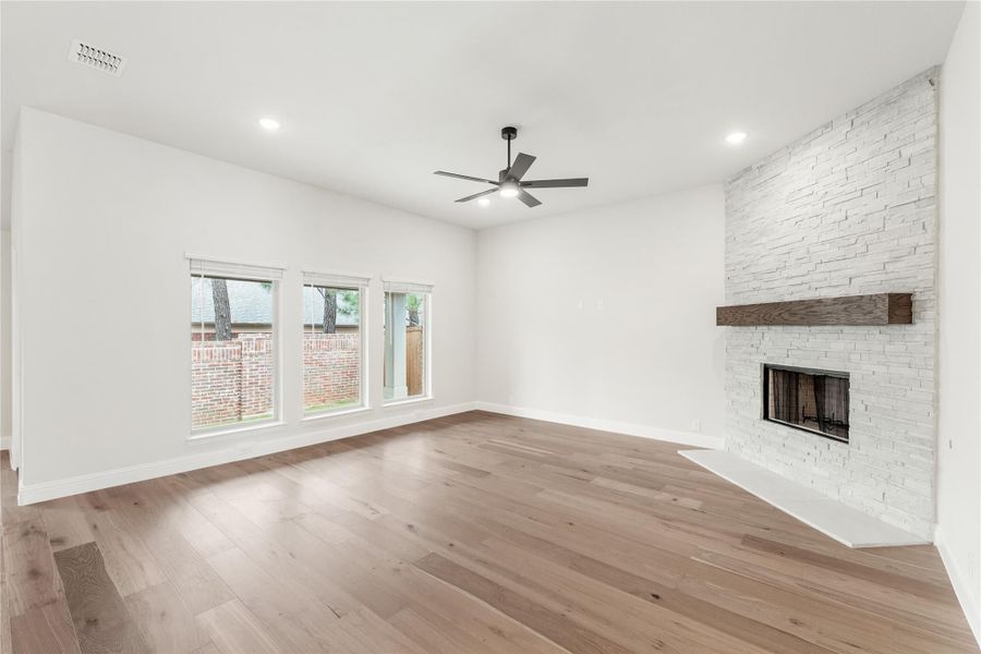 Open living room with hardwood floors, ceiling fan, and white stacked-stone fireplace with wood mantel
