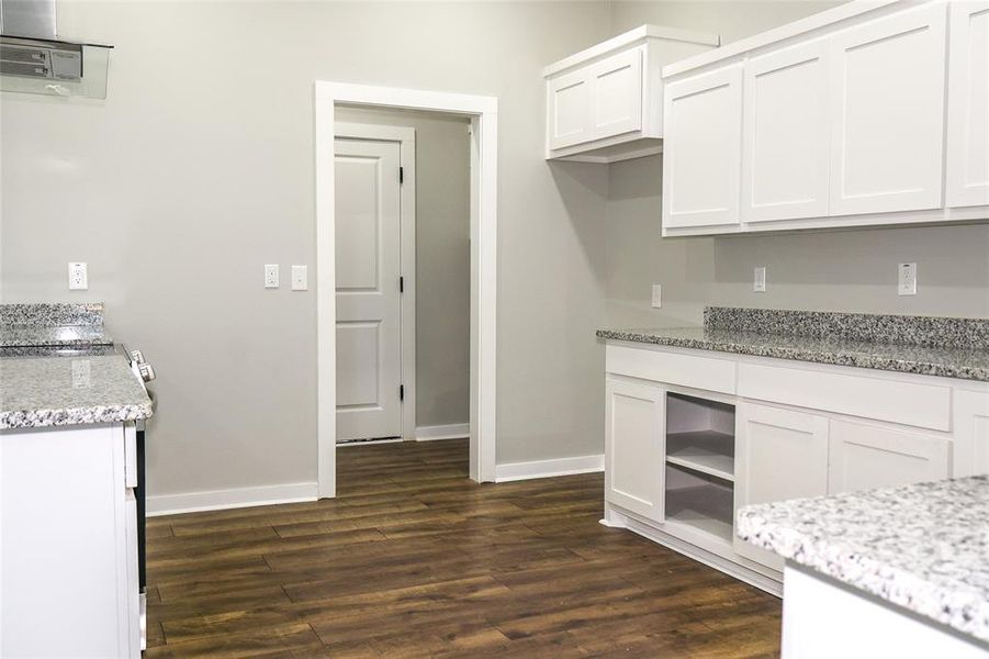 Kitchen featuring dark wood-type flooring, white cabinets, and light stone counters